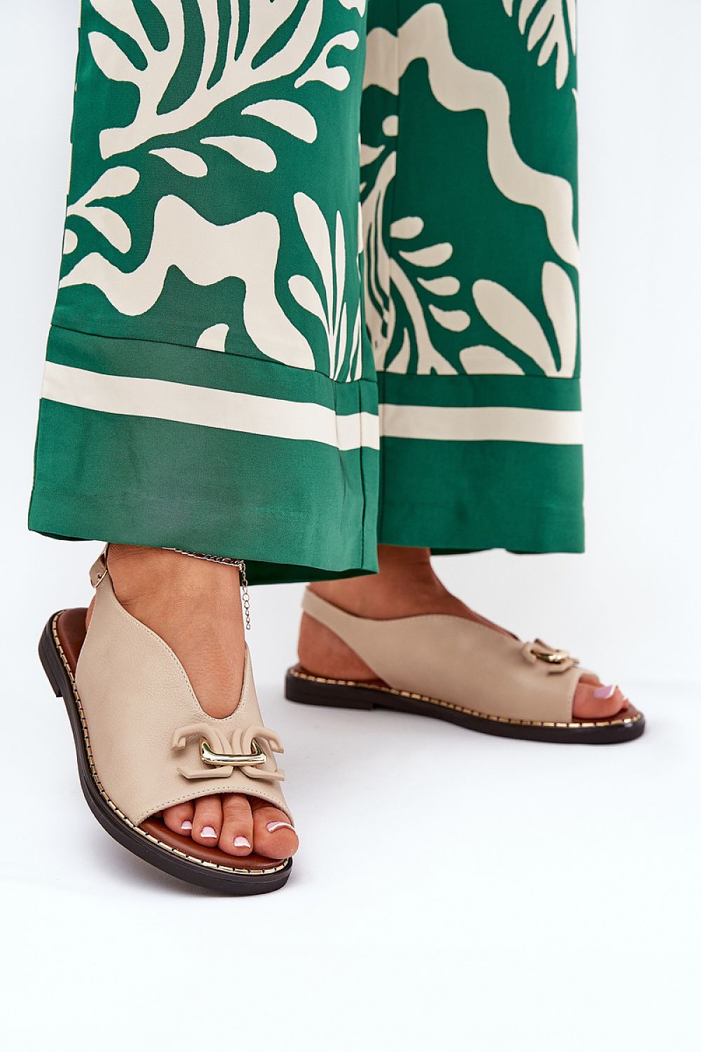 Woman wearing Almira Flat Eco-Leather Sandals with elegant design and subtle decorative front detail, paired with green patterned trousers.