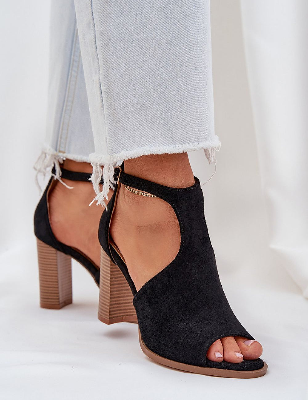 Black suede buckled heel sandals with adjustable ankle strap, styled with light denim jeans. Ideal for refined summer looks.