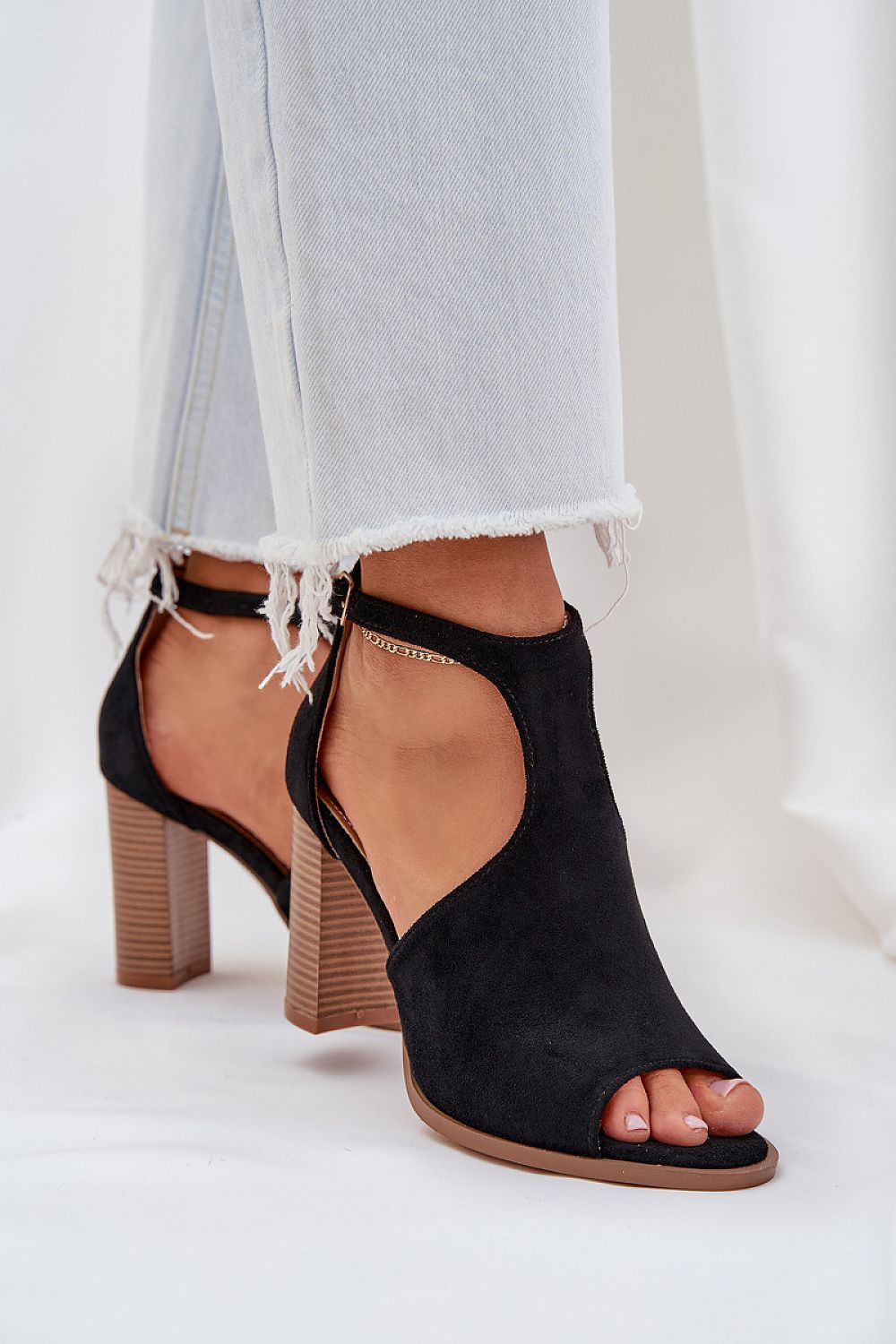 Black suede buckled heel sandals with adjustable ankle strap, styled with light denim jeans. Ideal for refined summer looks.