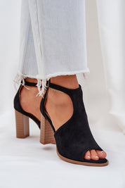 Black suede buckled heel sandals with adjustable ankle strap, styled with light denim jeans. Ideal for refined summer looks.
