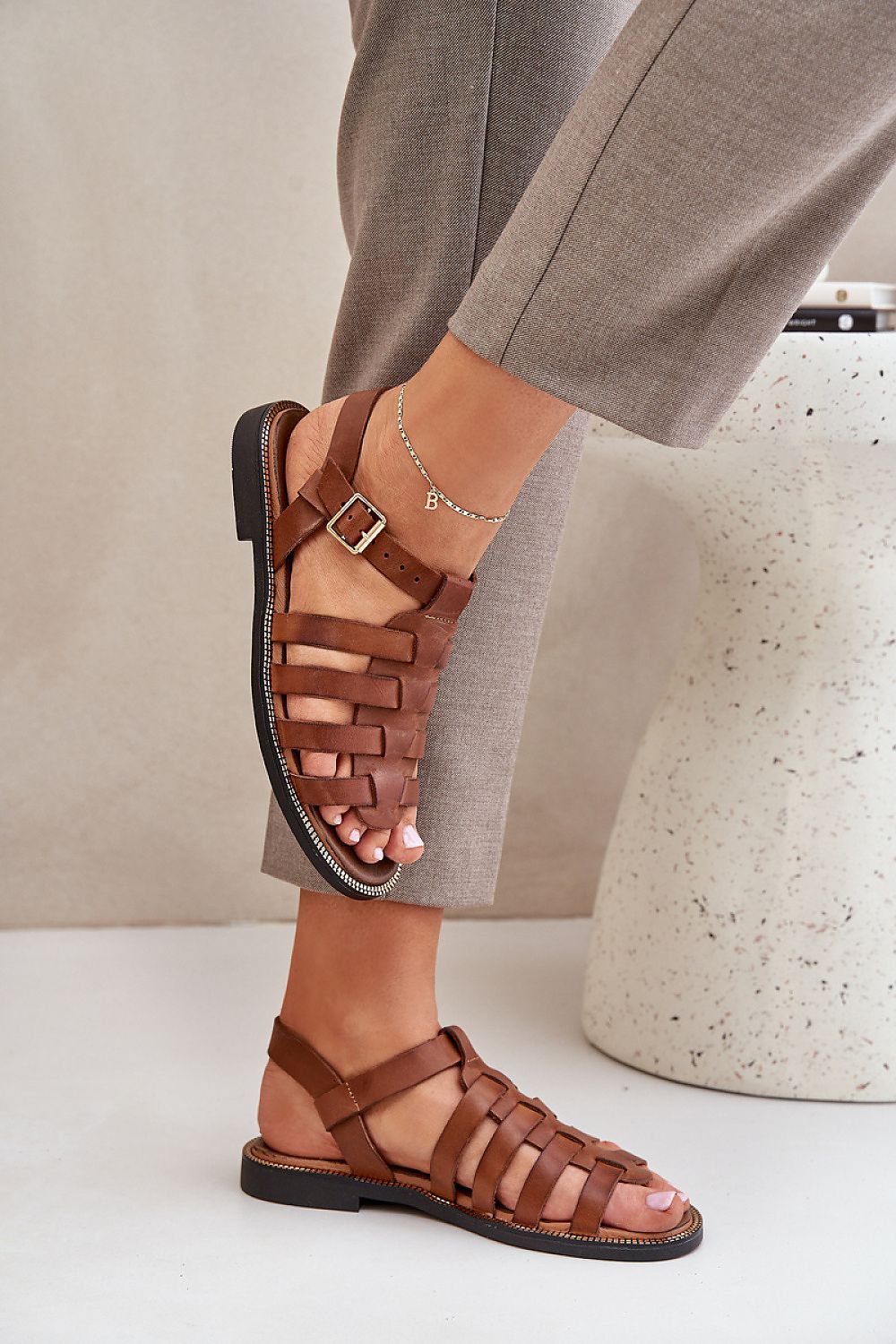 Woman wearing Celira Flat Leather Sandals with ankle buckle, showcasing genuine leather design and minimalist style against a neutral background.