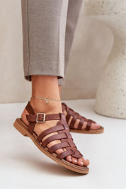 Woman wearing Celira Flat Leather Sandals with ankle buckle in brown, showcasing a sleek, elegant design perfect for versatile wear.
