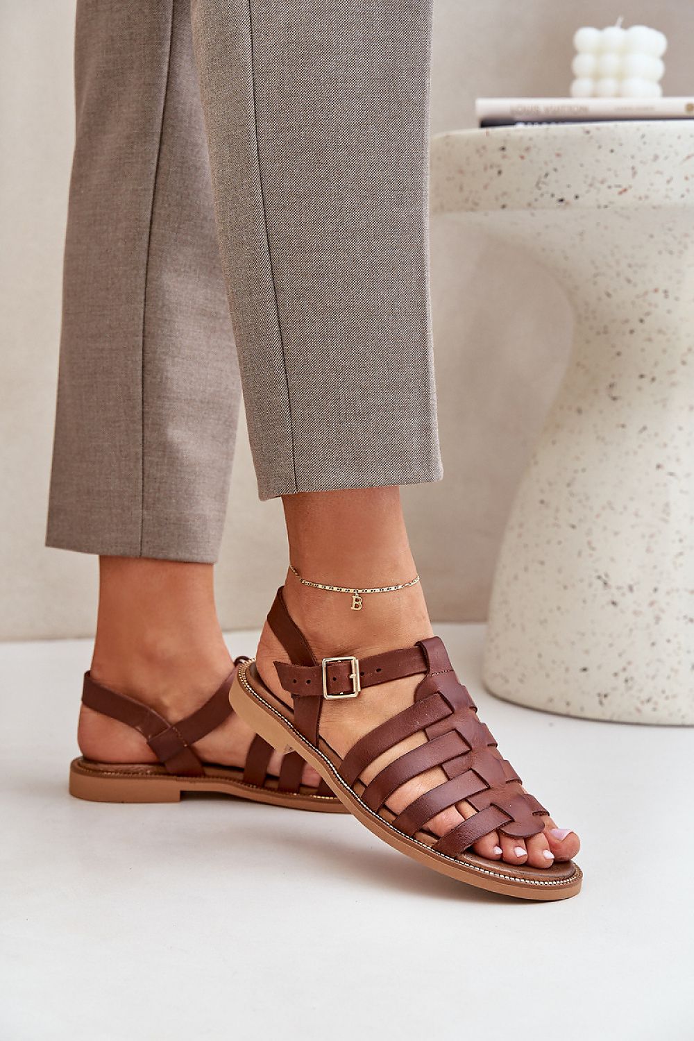 Woman wearing brown Celira Flat Leather Sandals with ankle buckle, showcasing minimalist design and genuine leather craftsmanship.