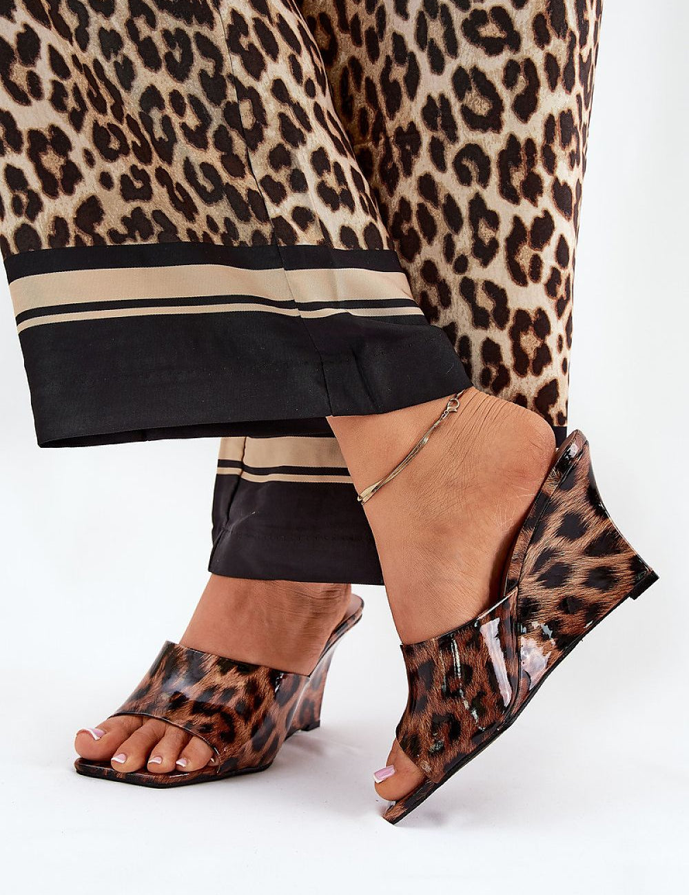Leopard print slip-on clogs with a tapered wedge heel, worn with matching leopard pattern trousers, showcasing chic summer fashion.