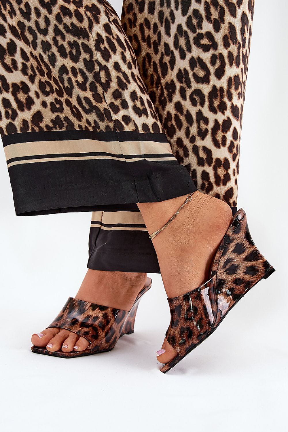 Leopard print slip-on clogs with a tapered wedge heel, worn with matching leopard pattern trousers, showcasing chic summer fashion.