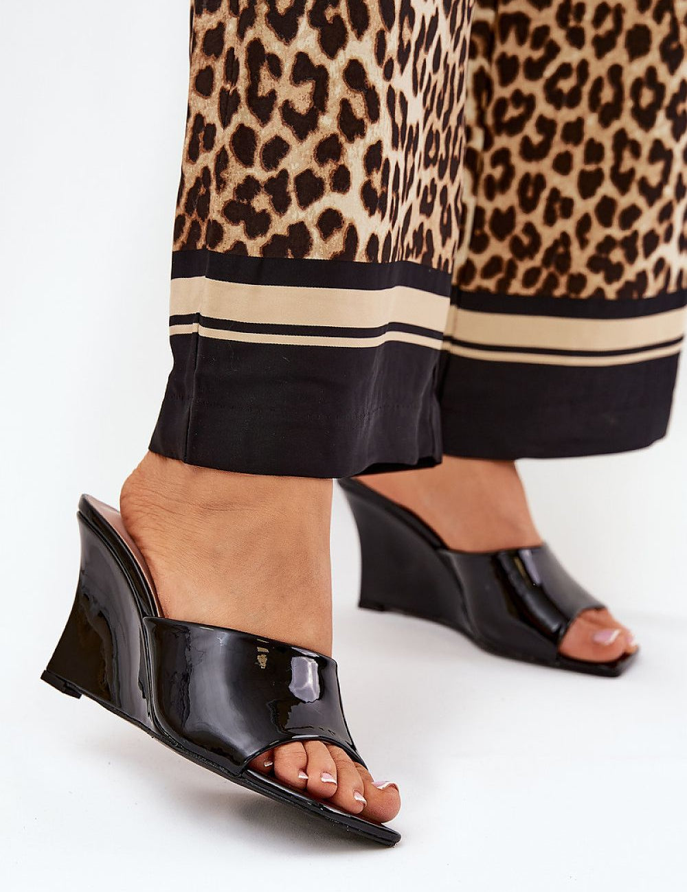 Woman wearing Solena Slip-On Summer Clogs with eco leather finish and wedge heel, paired with leopard print trousers.