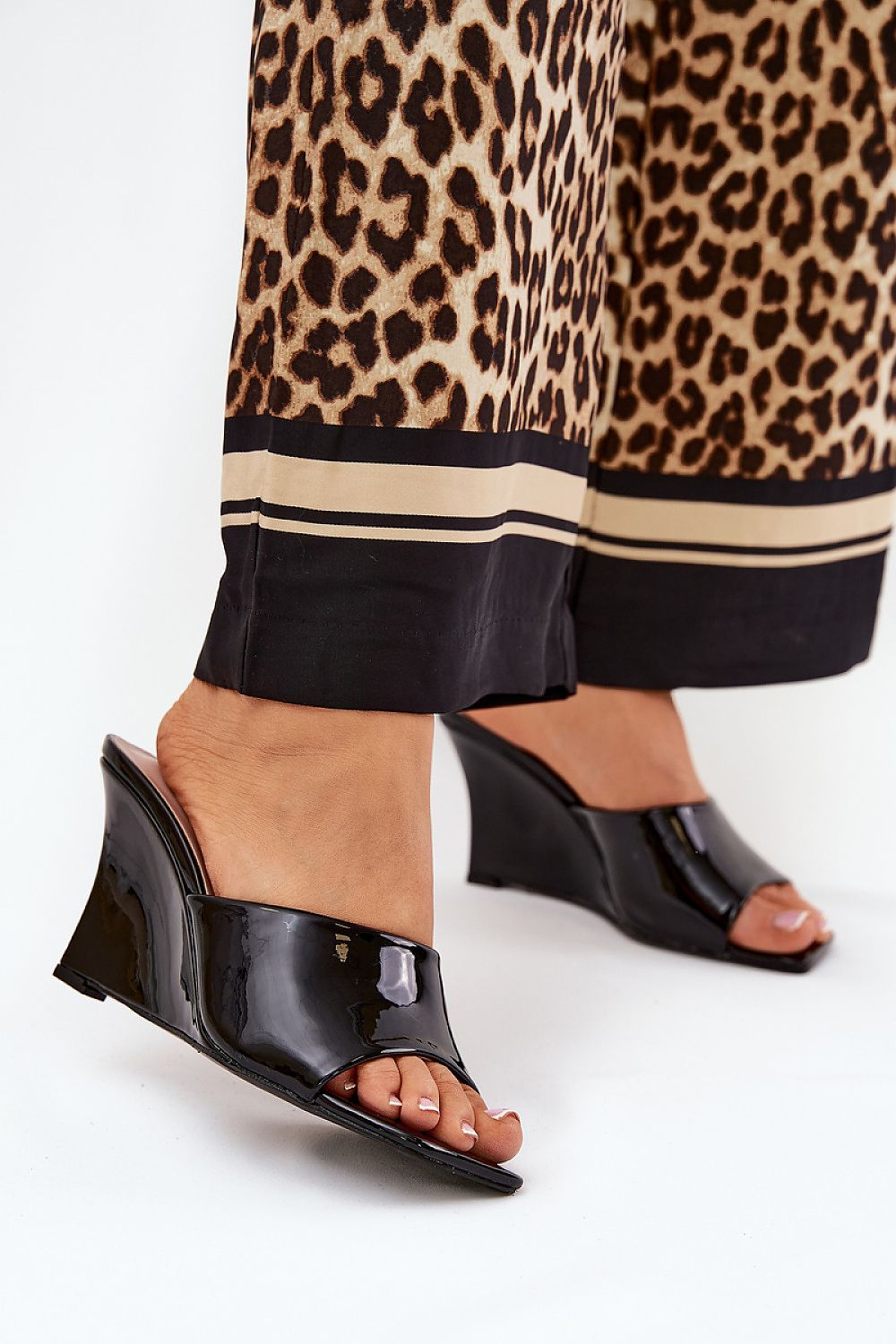 Woman wearing Solena Slip-On Summer Clogs with eco leather finish and wedge heel, paired with leopard print trousers.