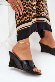Woman wearing black slip-on wedge clogs with eco leather finish and leopard print trousers, showcasing a chic summer style.