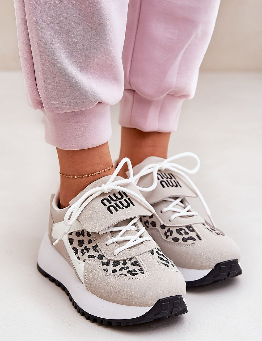 Comfortable white sneakers with leopard-print accents and white laces, paired with pink joggers for a stylish casual look.