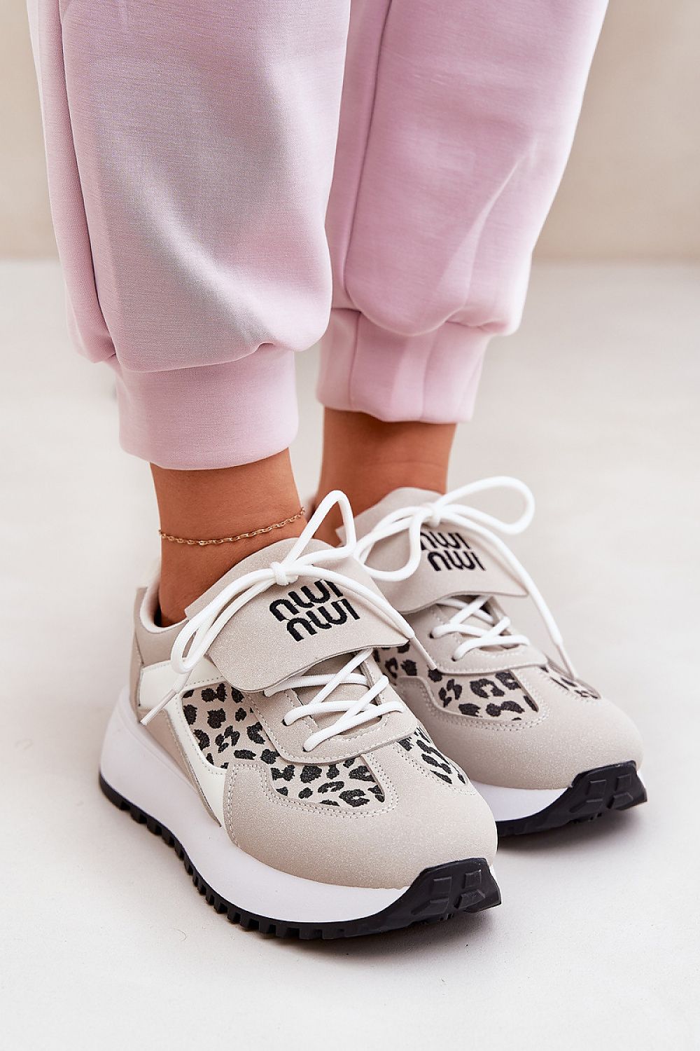 Comfortable white sneakers with leopard-print accents and white laces, paired with pink joggers for a stylish casual look.