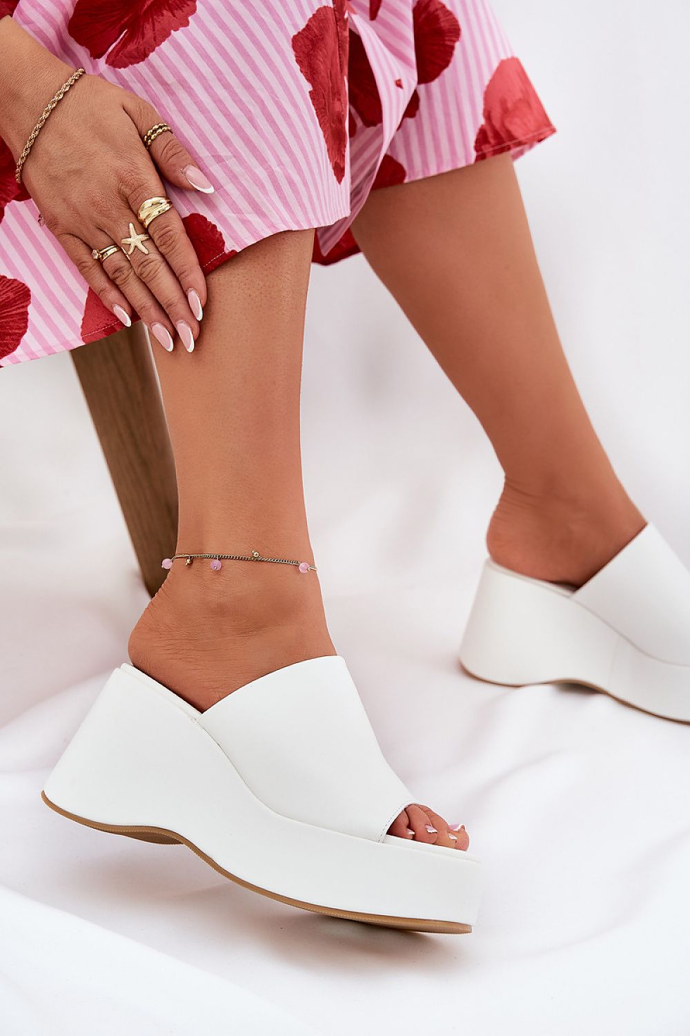 Woman wearing white wedge sandals with faux leather upper and pink floral dress, showcasing open-toe design and modern elegance.