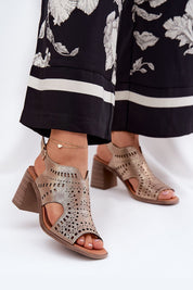 Woman wearing stylish cutout block heel sandals with ankle strap, accessorized with a delicate anklet, paired with floral print pants.