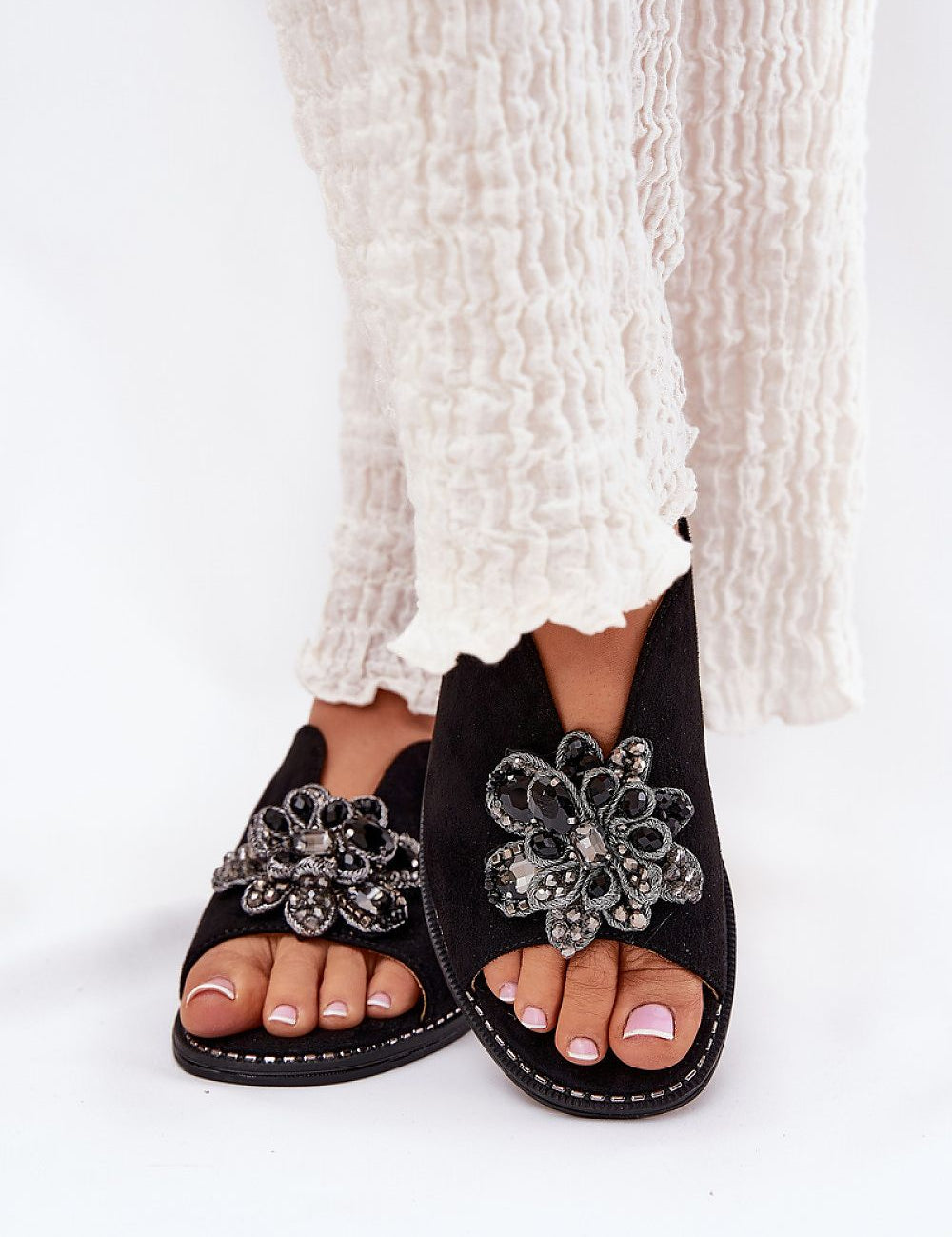 Fiorenna flat suede flower sandals with sculpted flower accent and cushioned insole, paired with flowing light fabric trousers.