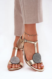 Woman wearing gold Evelenne leather sandals with sculpted heel and decorative front accents.