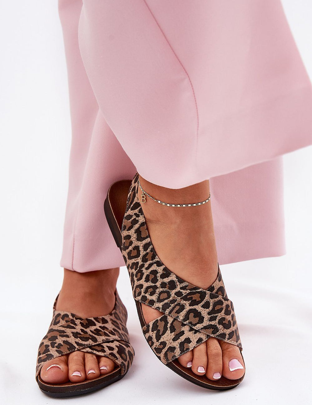 Leopard print leather sandals with soft straps and open heel, paired with pink trousers, showcasing elegant and breathable summer footwear.