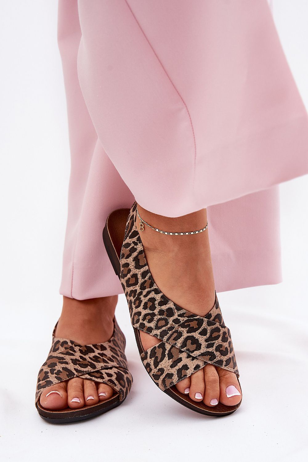Leopard print leather sandals with soft straps and open heel, paired with pink trousers, showcasing elegant and breathable summer footwear.