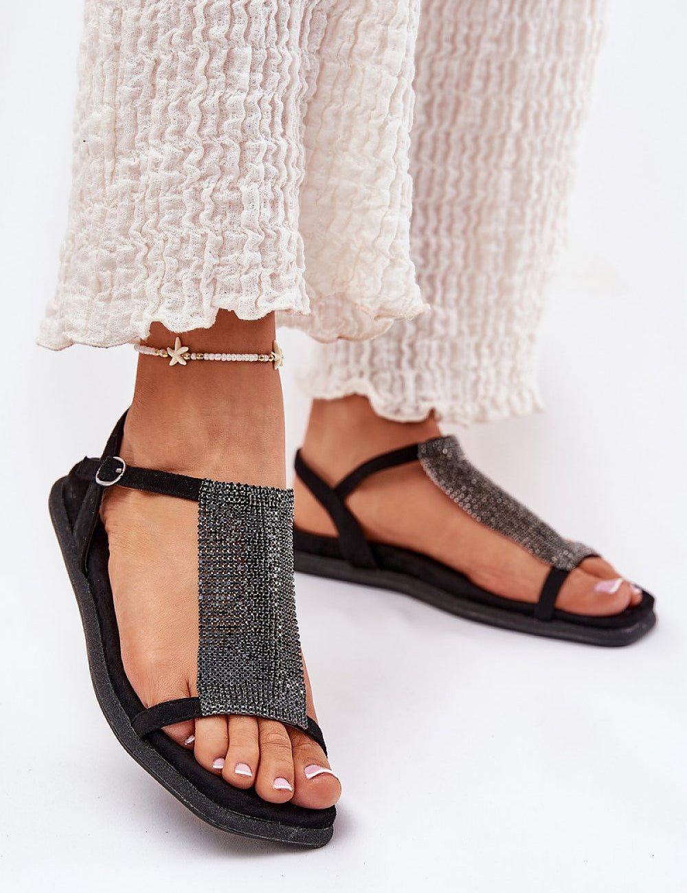 Woman wearing Cirellane Crystal Strap Sandals in black with imitation suede, showing crystal-adorned straps and adjustable buckle.