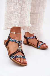 Close-up of Aviretta Braided Zircon Sandals with braided straps and zircon accents, worn with white textured pants.
