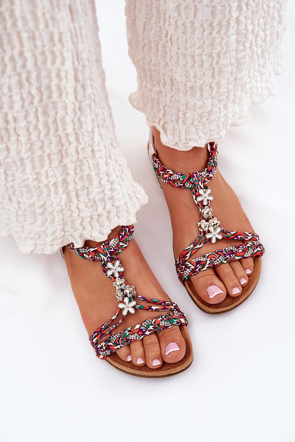 Person wearing Zirellia Woven Flat Sandals with colorful braided straps and floral embellishments, perfect for summer.