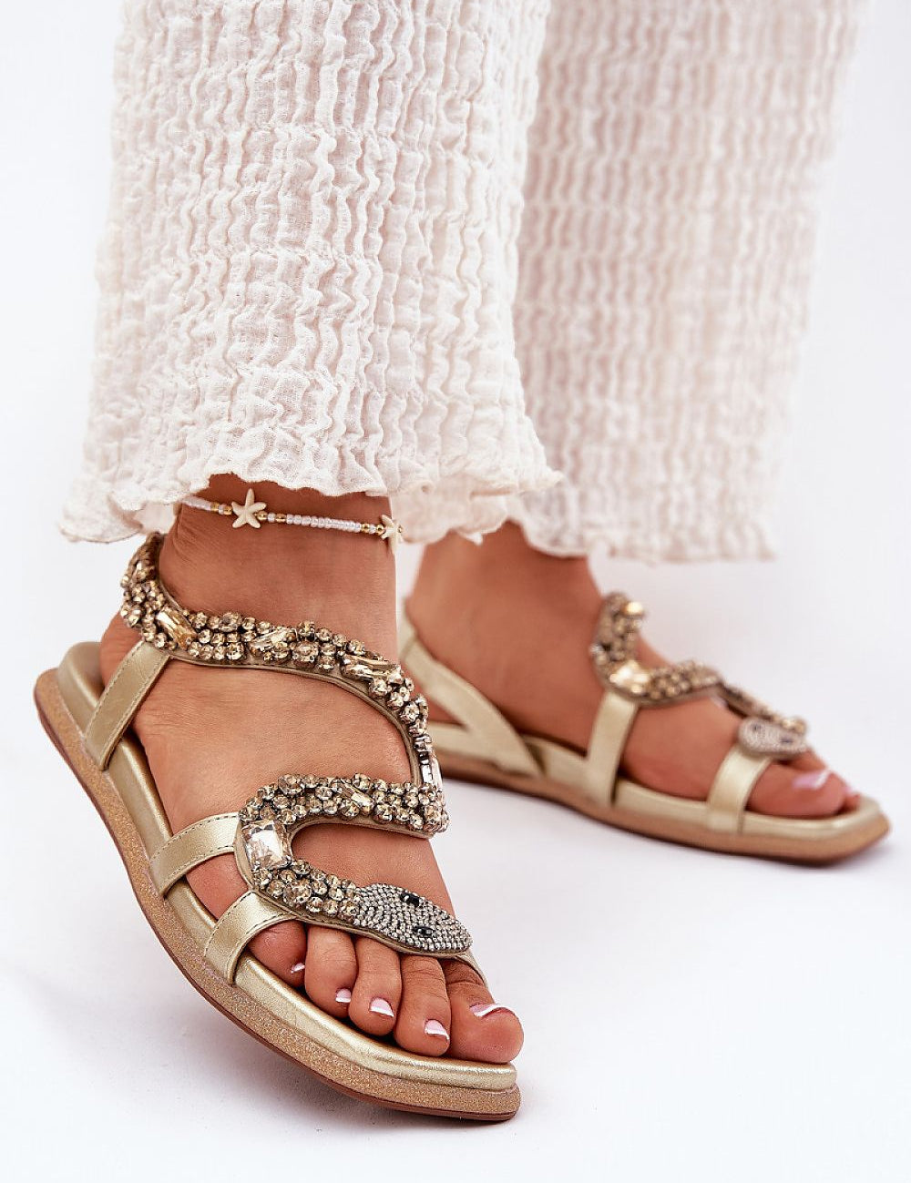 Nevalia Sandals with Crystal Snake Detail, featuring eco-leather and sequin-trimmed sole, worn with white pants, perfect for summer style.