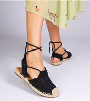 Woman wearing Serella Espadrille Sandals with a braided sole and black fabric, styled with a floral skirt for a summer look.