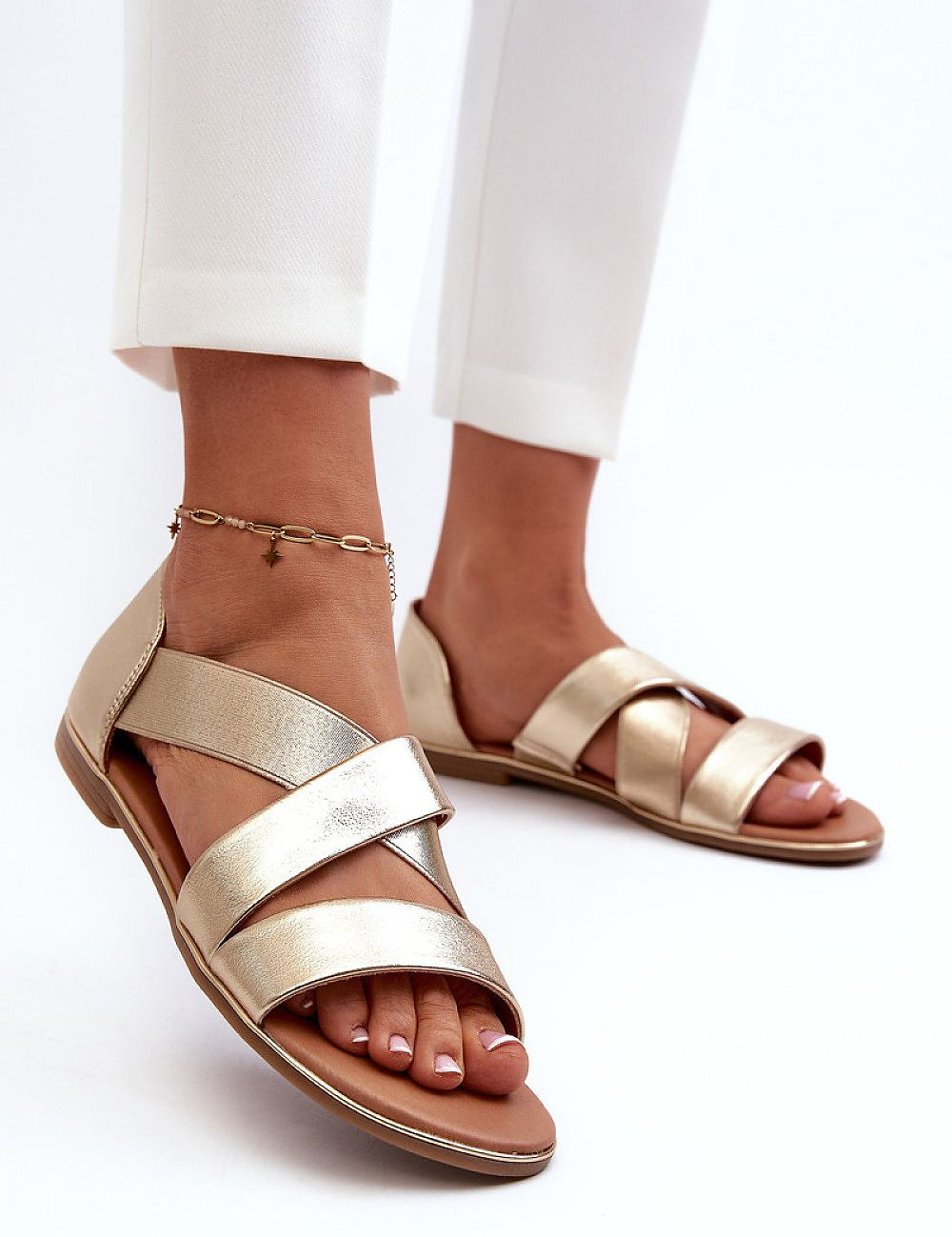 Woman wearing Zirella Elastic Strap Sandals in gold, featuring a sleek minimalist design with synthetic upper and supportive elastic strap.