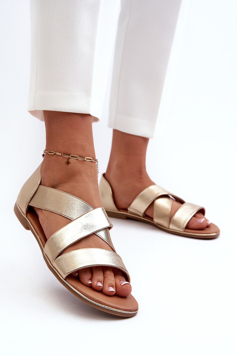 Woman wearing Zirella Elastic Strap Sandals in gold, featuring a sleek minimalist design with synthetic upper and supportive elastic strap.