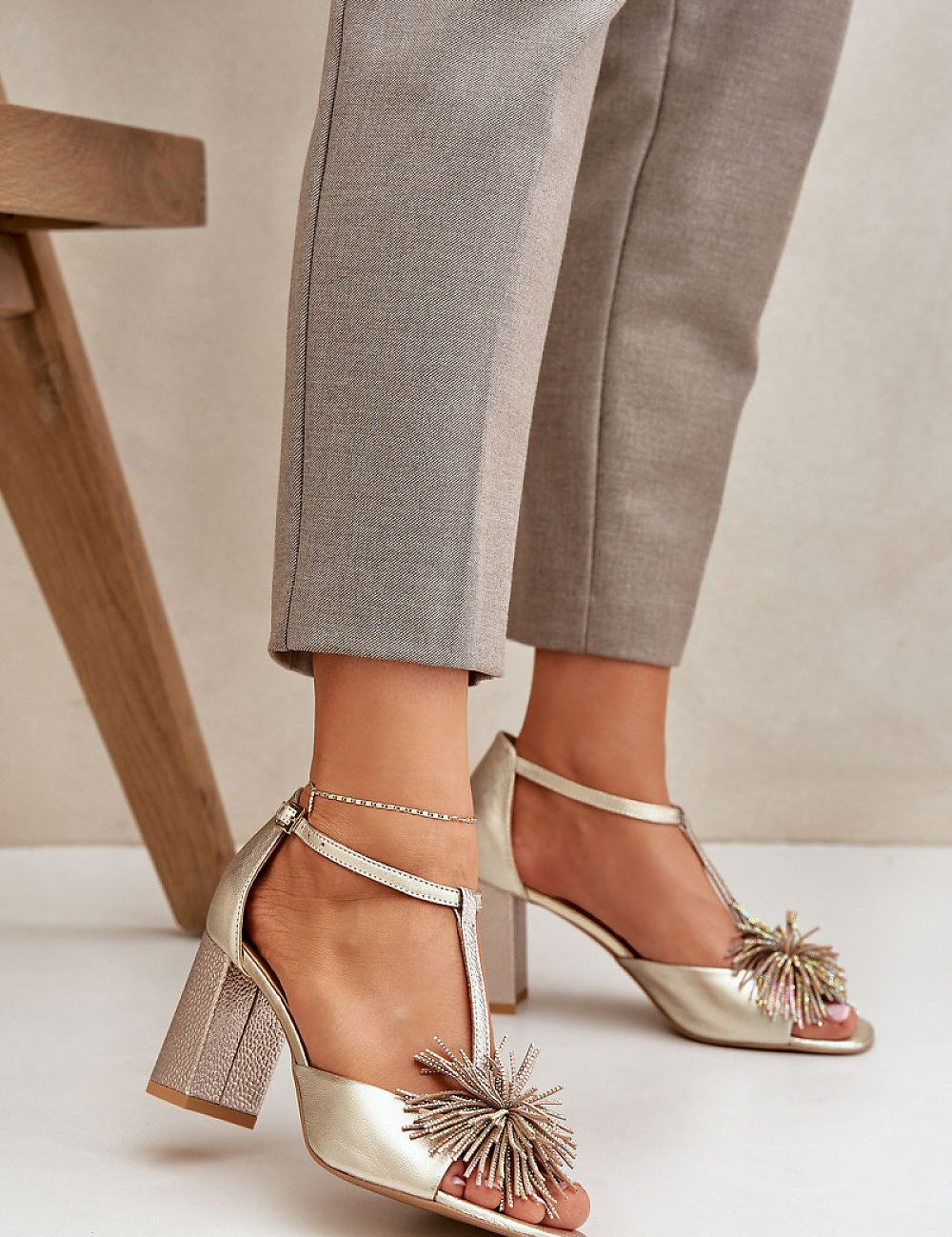 Woman wearing Tirelda Leather Column Heel Sandals with decorative front accent and adjustable strap, paired with gray trousers.