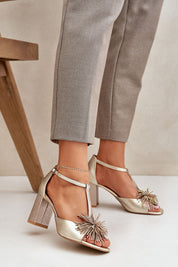 Woman wearing Tirelda Leather Column Heel Sandals with decorative front accent and adjustable strap, paired with gray trousers.