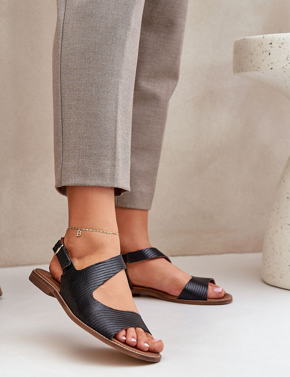 Person wearing Zaniva Flat Leather Sandals with ankle strap and buckle, styled with neutral pants, emphasizing comfort and refined simplicity.