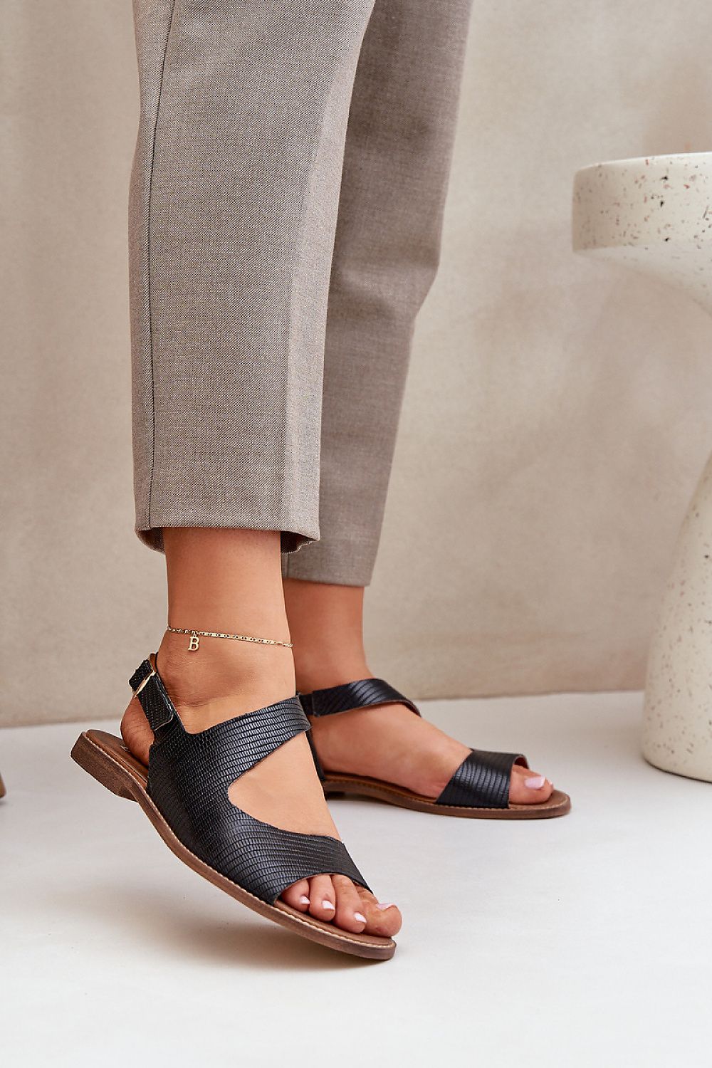 Person wearing Zaniva Flat Leather Sandals with ankle strap and buckle, styled with neutral pants, emphasizing comfort and refined simplicity.