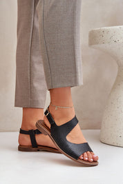 Woman wearing Zaniva flat leather sandals with adjustable ankle strap, featuring minimal design and classic buckle fastening.