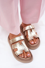 Gold platform strap sandals on feet, paired with pink pants, featuring perforated design and thick soles