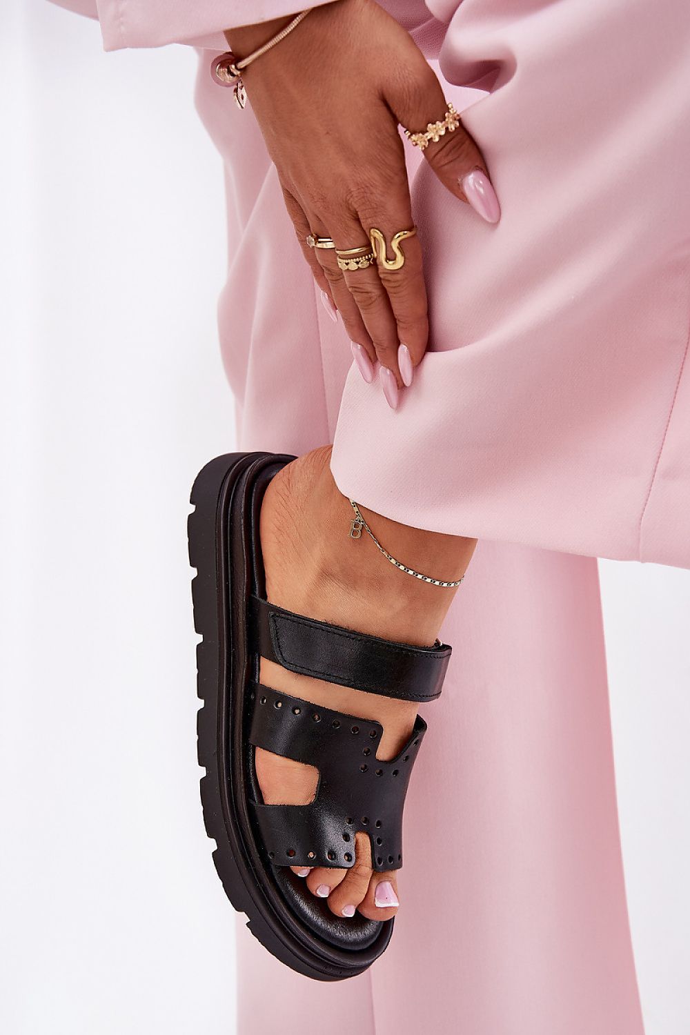 Black Mavena platform strap sandal on a woman's foot, showcasing contemporary design and comfort during a casual pose in pink pants.