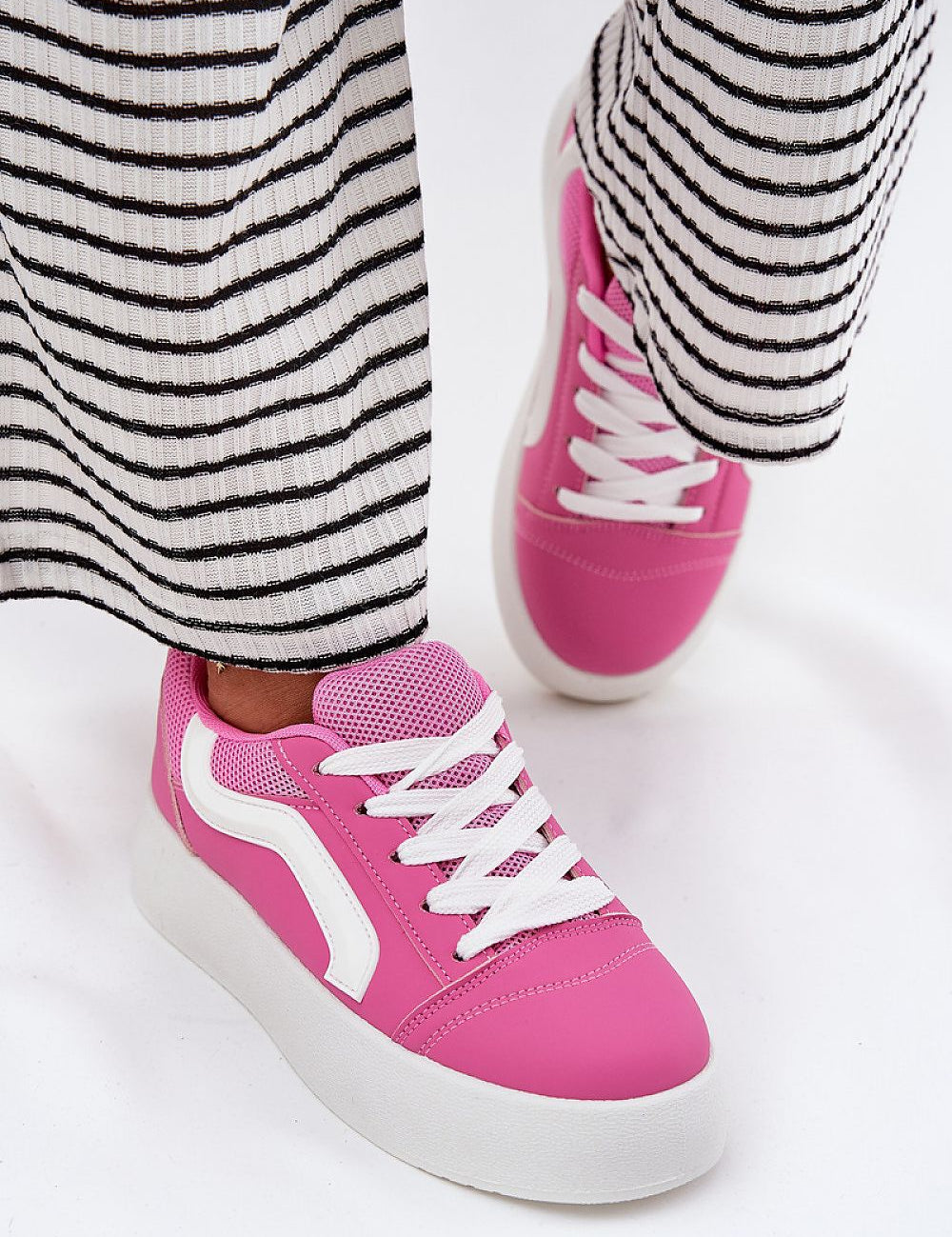 Woman wearing pink Ravelin Suede Platform Sneakers with a striped skirt, showcasing the eco-suede design and supportive platform sole.