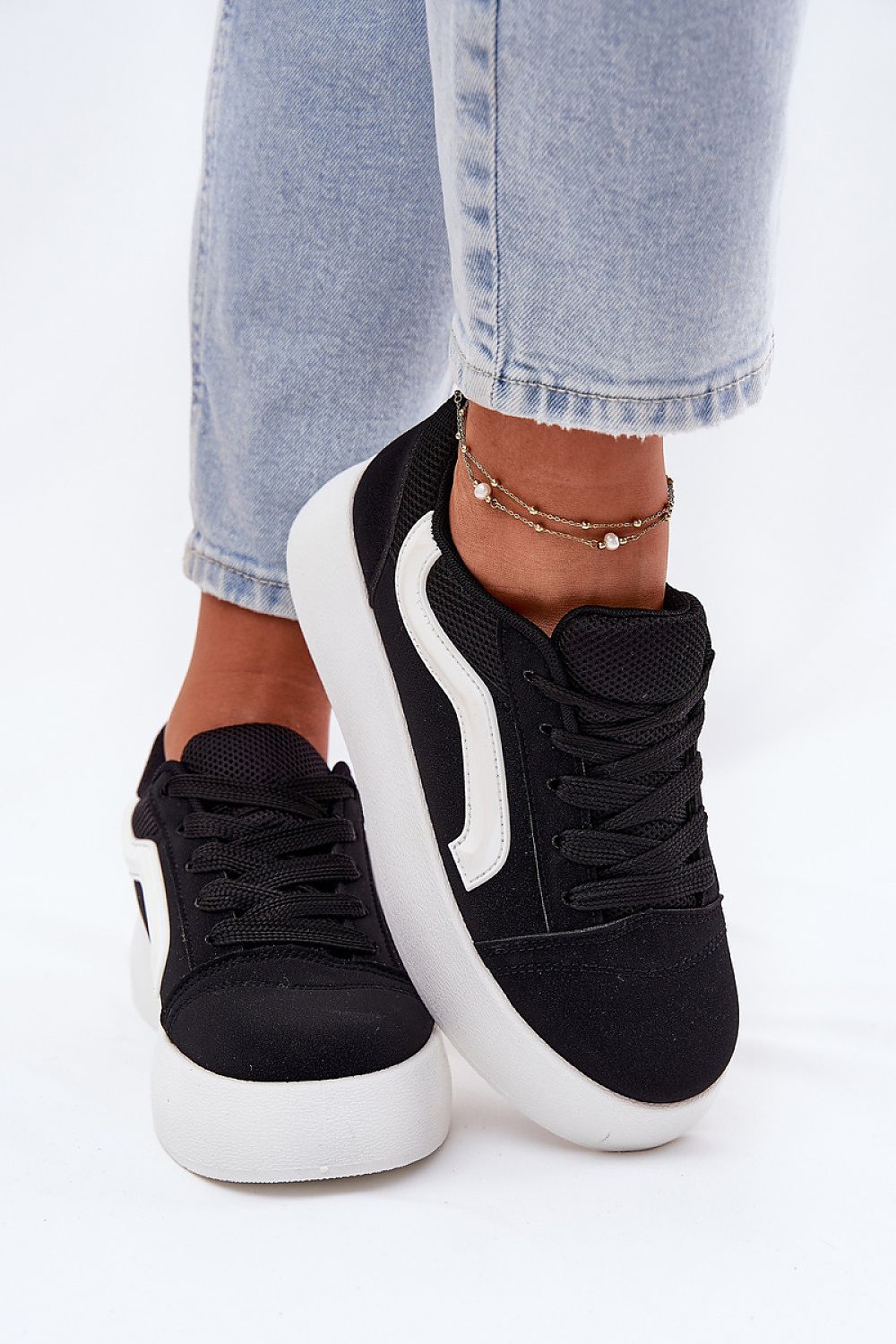 Black suede platform sneakers with white sole, worn with light-wash denim jeans, showcasing versatile and chic footwear style.