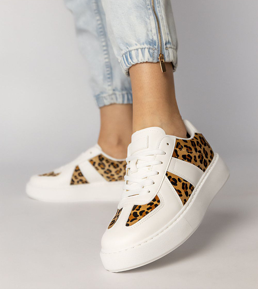 White platform sneakers with panther pattern and lace-up closure, crafted in synthetic leather, worn with rolled-up denim.