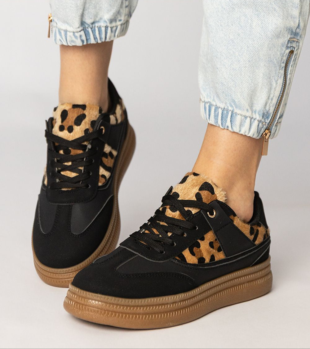 Black sneakers with leopard print detail and platform sole, paired with light denim jeans, showcasing a stylish and bold look.