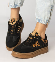 Black sneakers with leopard print detail and platform sole, paired with light denim jeans, showcasing a stylish and bold look.