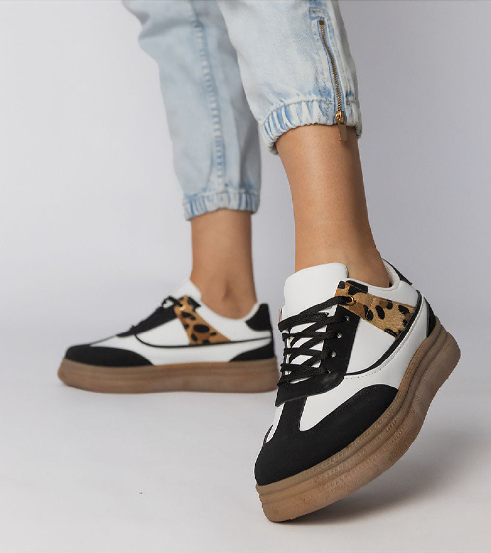 Woman wearing Merisse Panther Accent Sneakers, featuring white base and subtle panther print, with jeans.