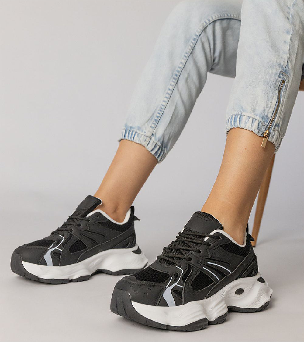 Black Thareen platform trainers with chunky sole and faux leather upper, worn with rolled jeans, offering bold urban style and comfort.