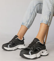 Black Thareen platform trainers with chunky sole and faux leather upper, worn with rolled jeans, offering bold urban style and comfort.