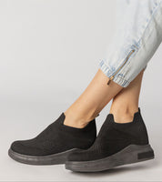 Black shadowknit slip-on sock sneakers with stretch-knit upper and firm platform sole, styled with light jeans showcasing zip detail.