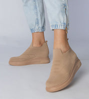 Beige slip-on sock sneakers with stretch-knit upper and platform sole, paired with light blue jeans for an urban chic look.