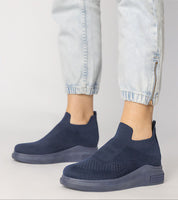 Shadowknit Slip-On Sock Sneakers in navy, featuring a stretch-knit upper and platform sole, styled with light-wash jogger pants.