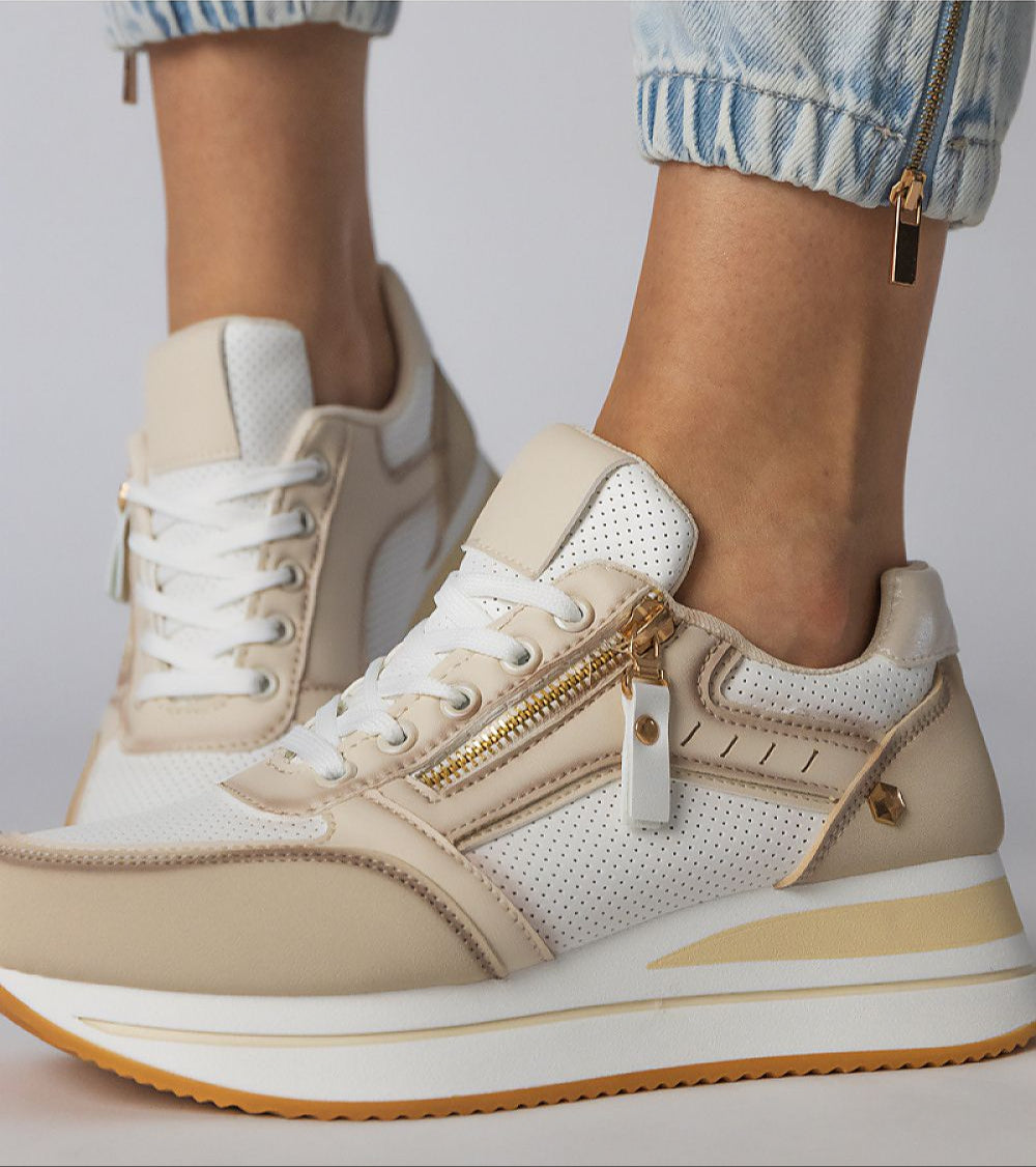 Women's beige and white sneakers with side zippers and a platform sole, paired with light blue jeans.