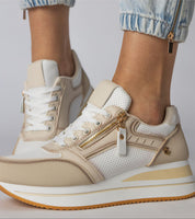 Women's beige and white sneakers with side zippers and a platform sole, paired with light blue jeans.