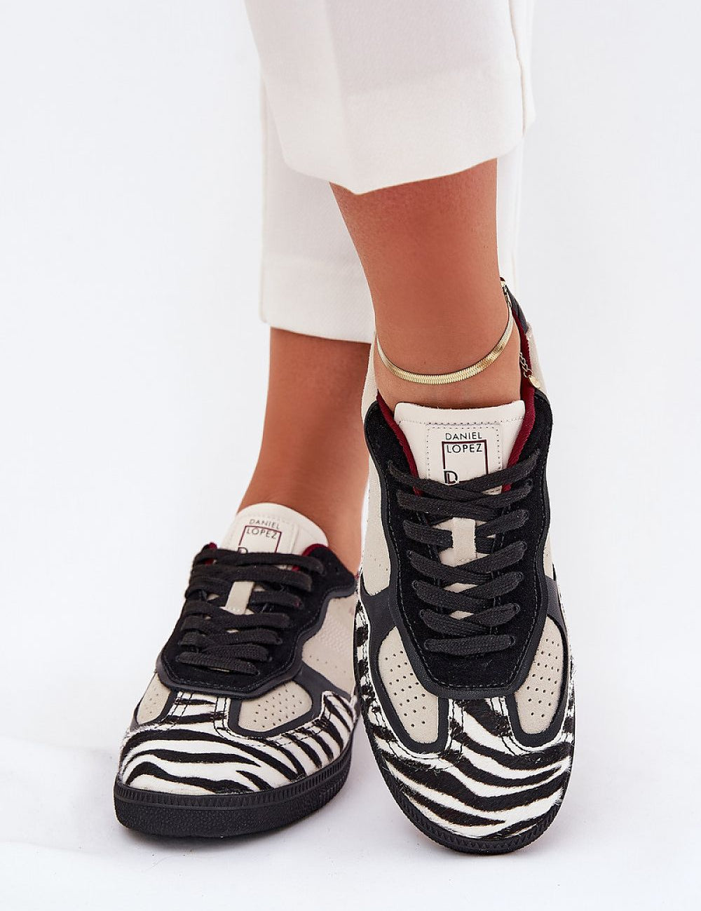 Black and white zebra-patterned sneakers paired with white pants, showcasing stylish and unique footwear design.