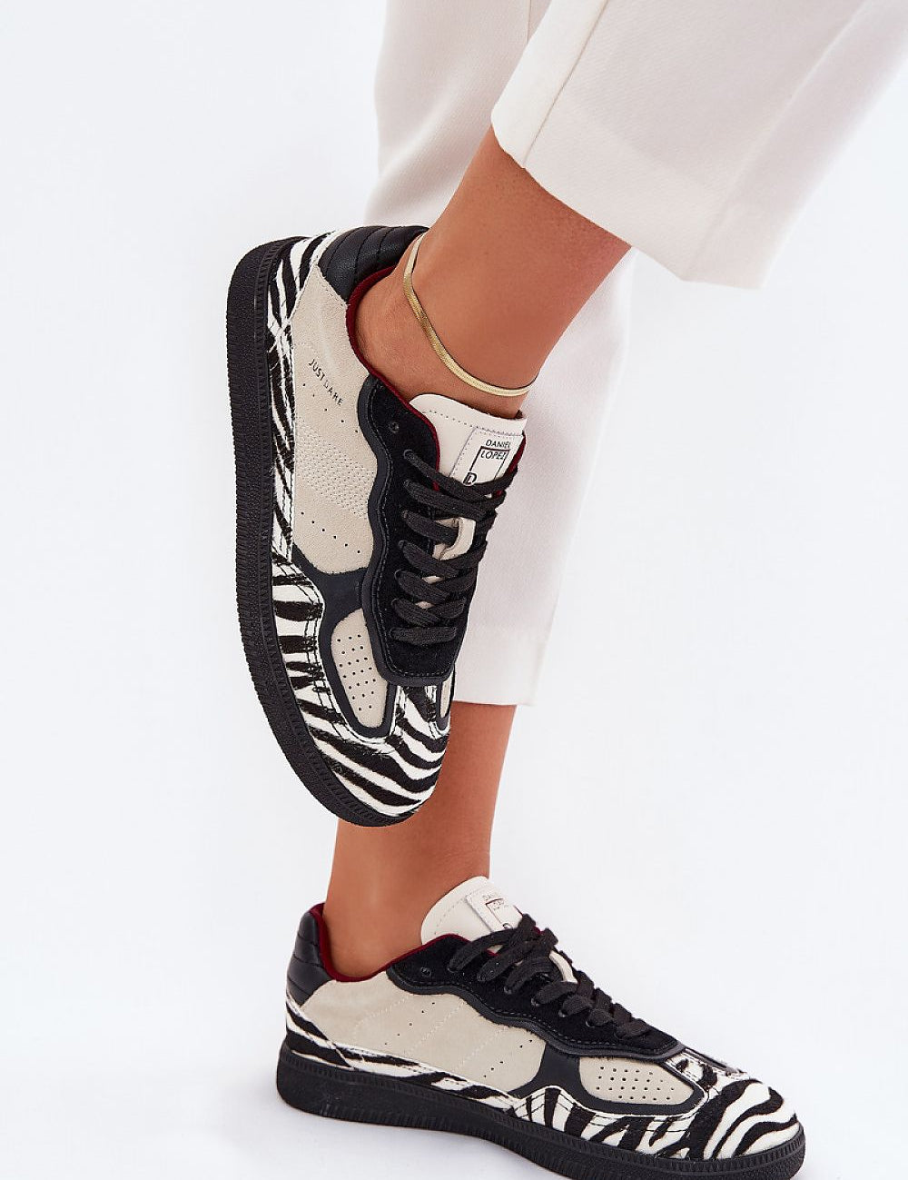 Zebra-pattern sneakers with black laces and white soles, paired with white pants, showcasing modern style and urban edge.
