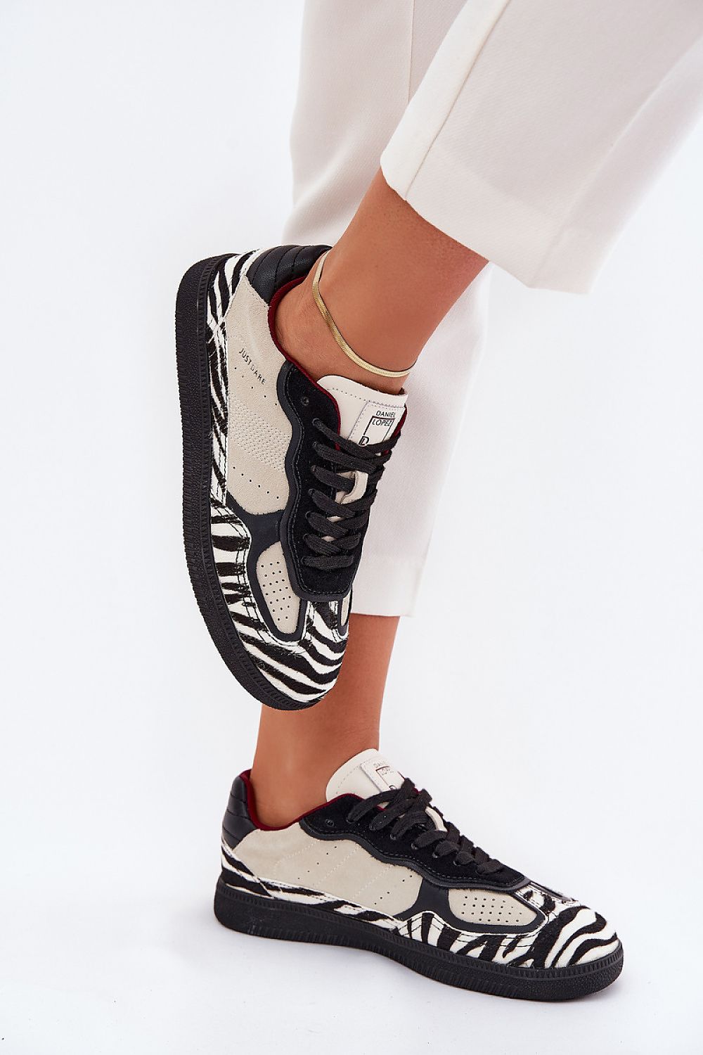 Zebra-pattern sneakers with black laces and white soles, paired with white pants, showcasing modern style and urban edge.